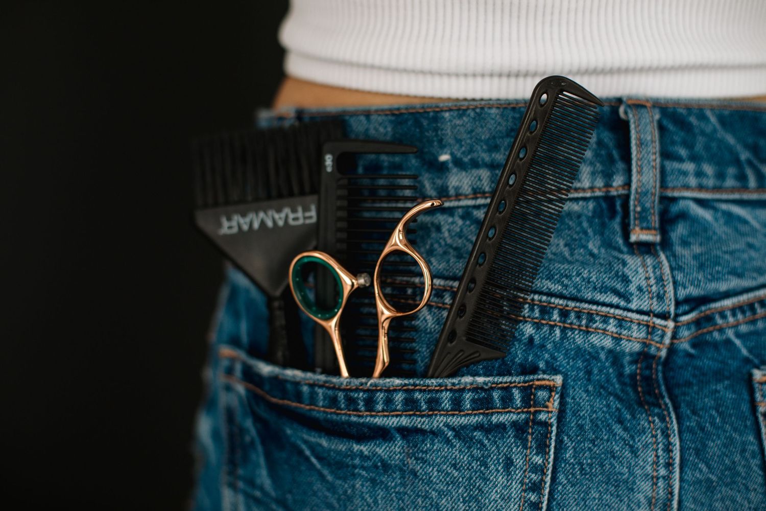 Close-up of Framar comb and gold scissors tucked into the back pocket of blue denim jeans.