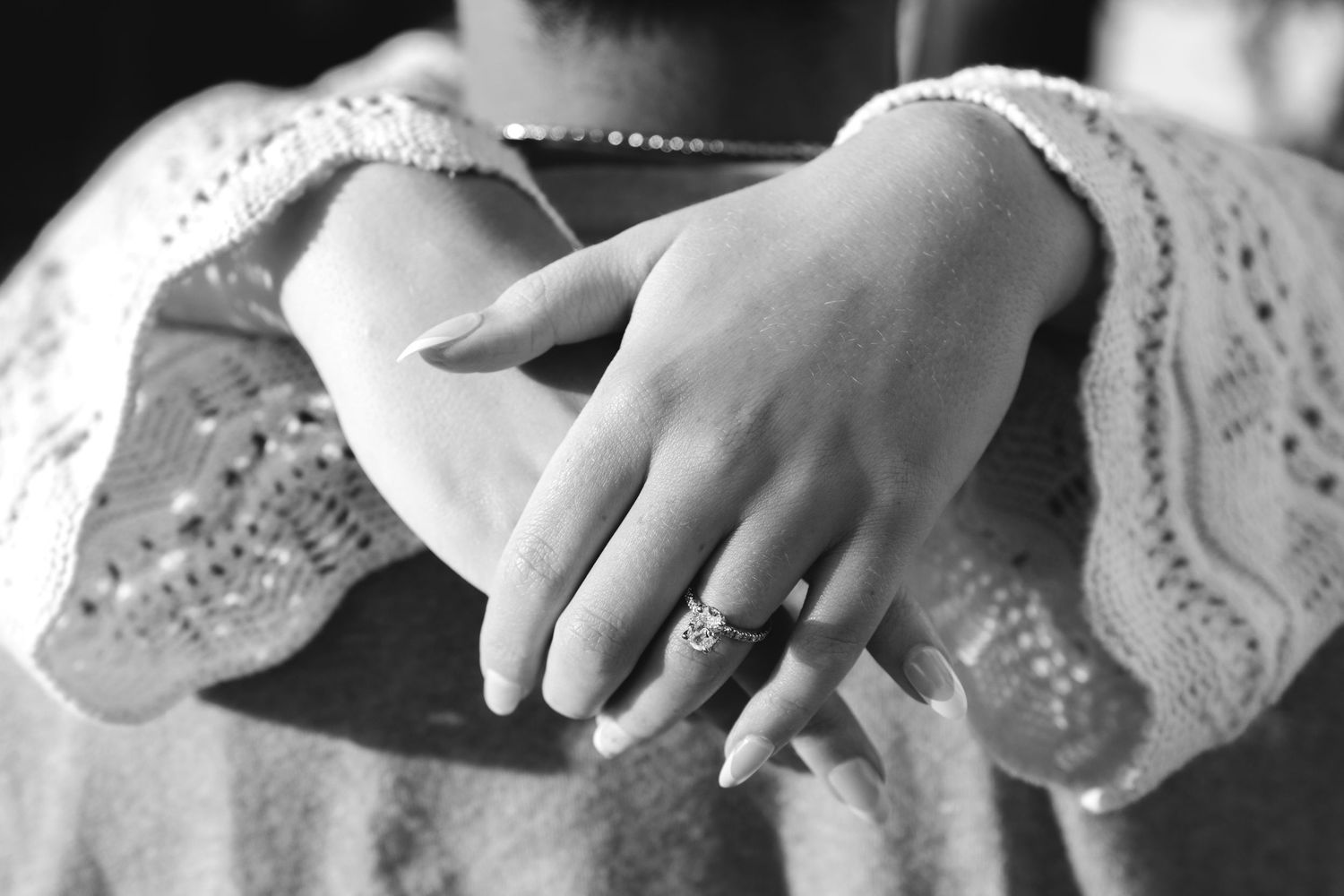 Black and white close-up of a woman's hands wearing a delicate ring, with lace sleeve cuffs visible.
