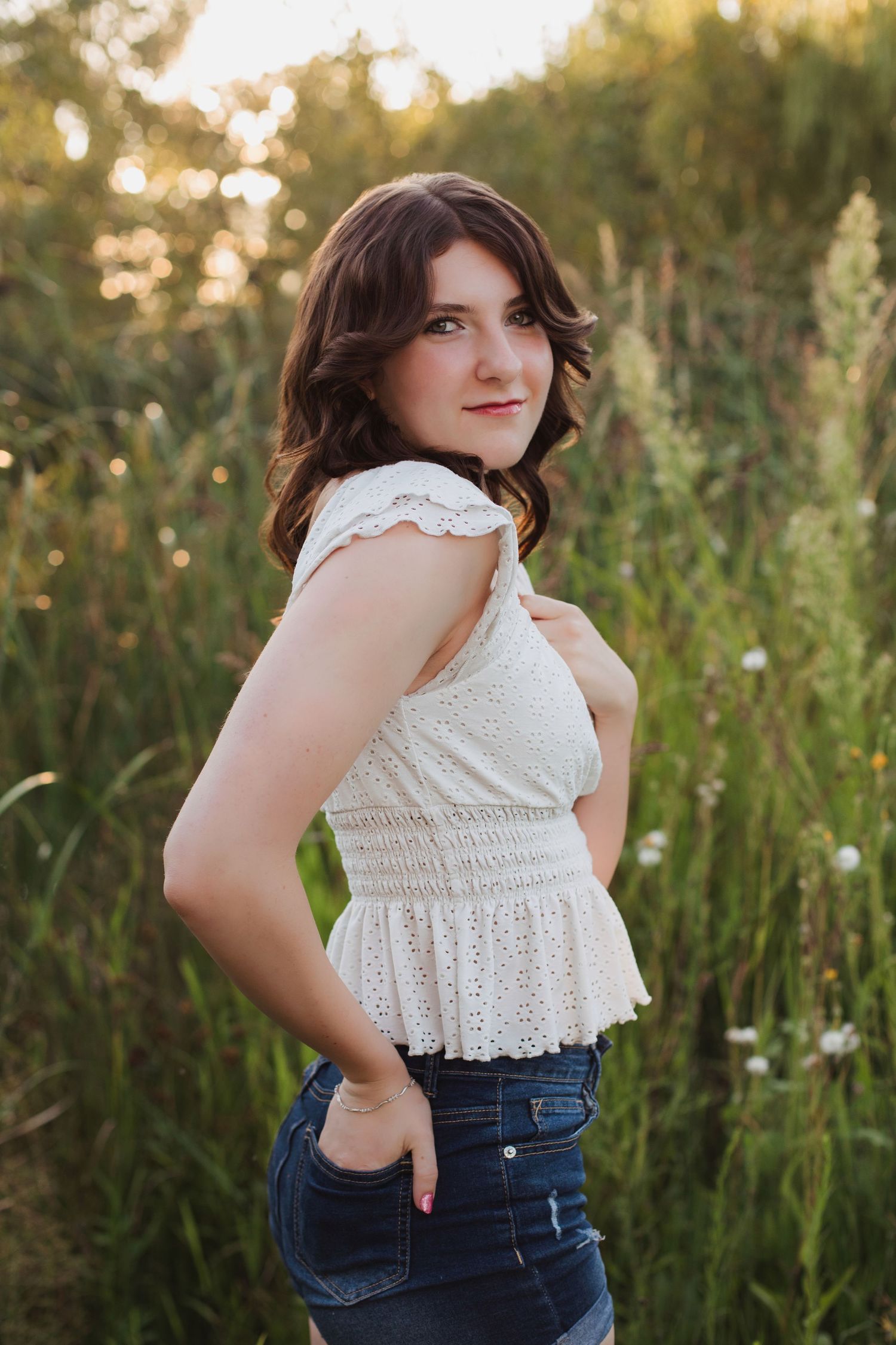 Teen girl in white lace top and jeans in green field.
