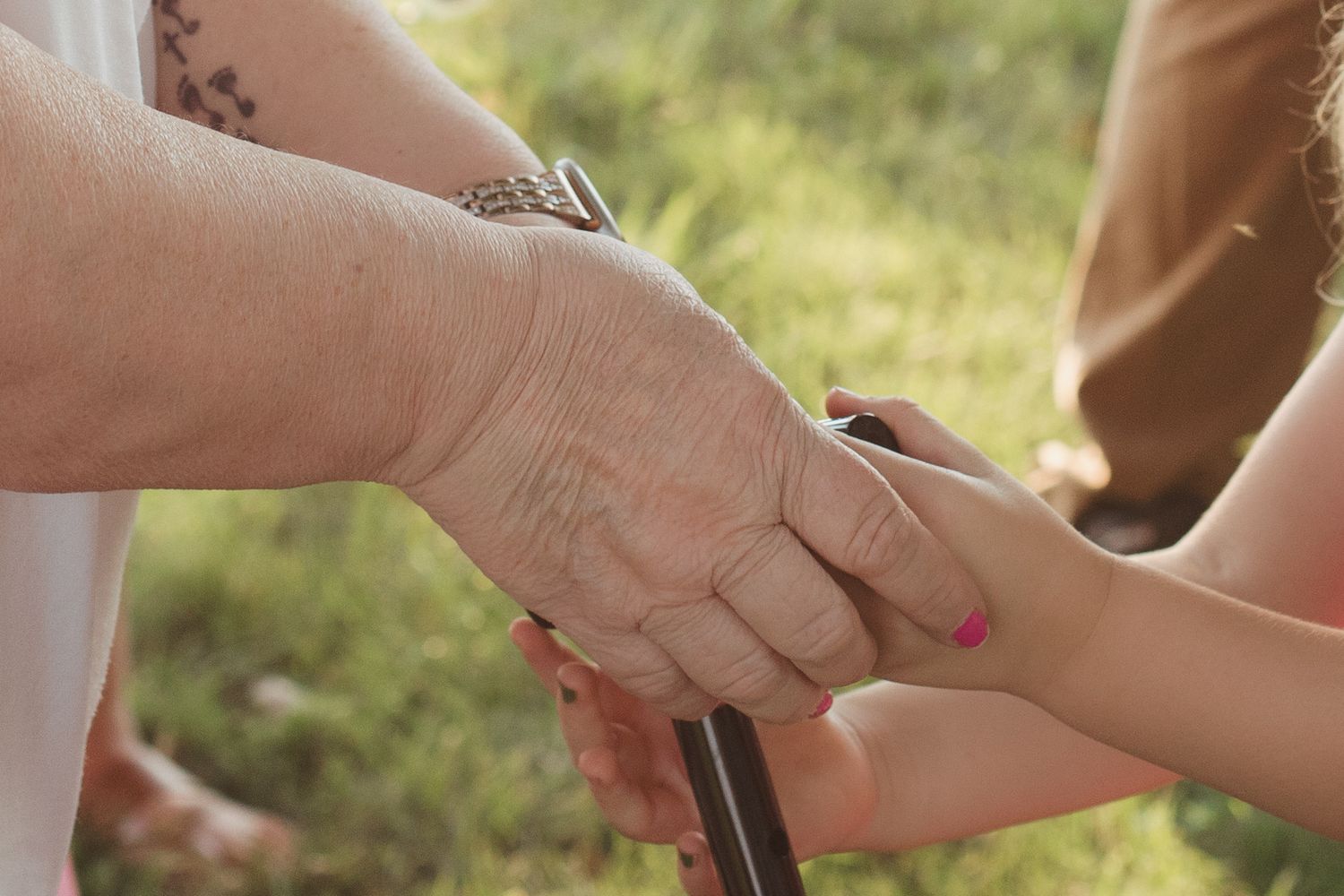Close-up of elderly hands holding a young childs hand with pink nails outdoors.