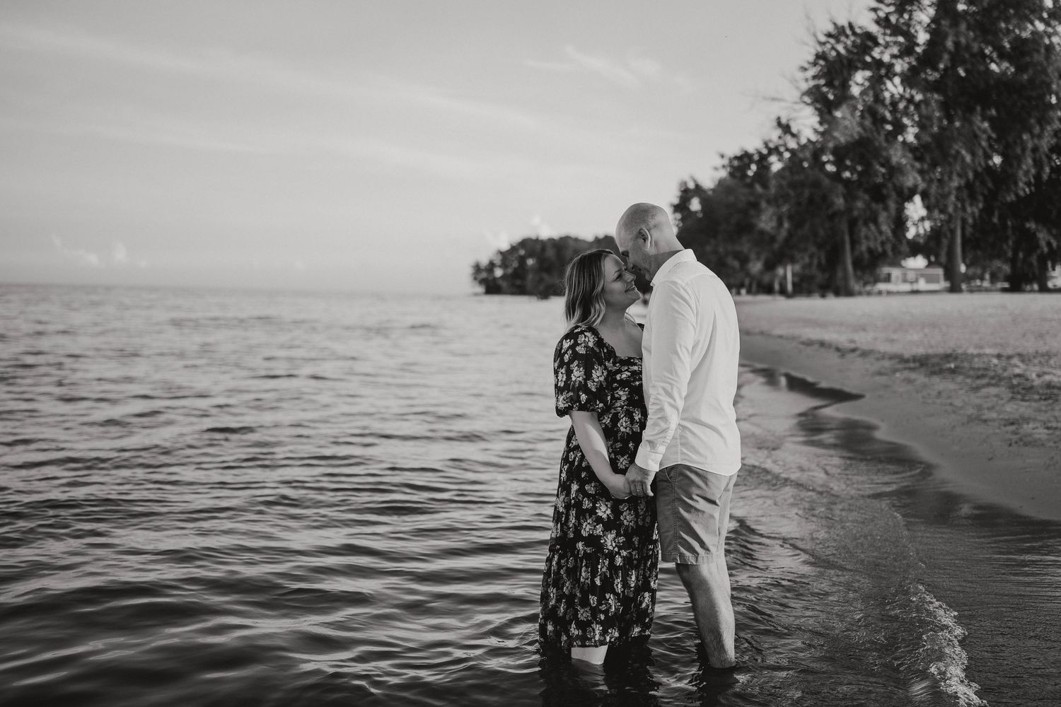 Black and white photo of a romantic couple standing face to face in shallow beach water.