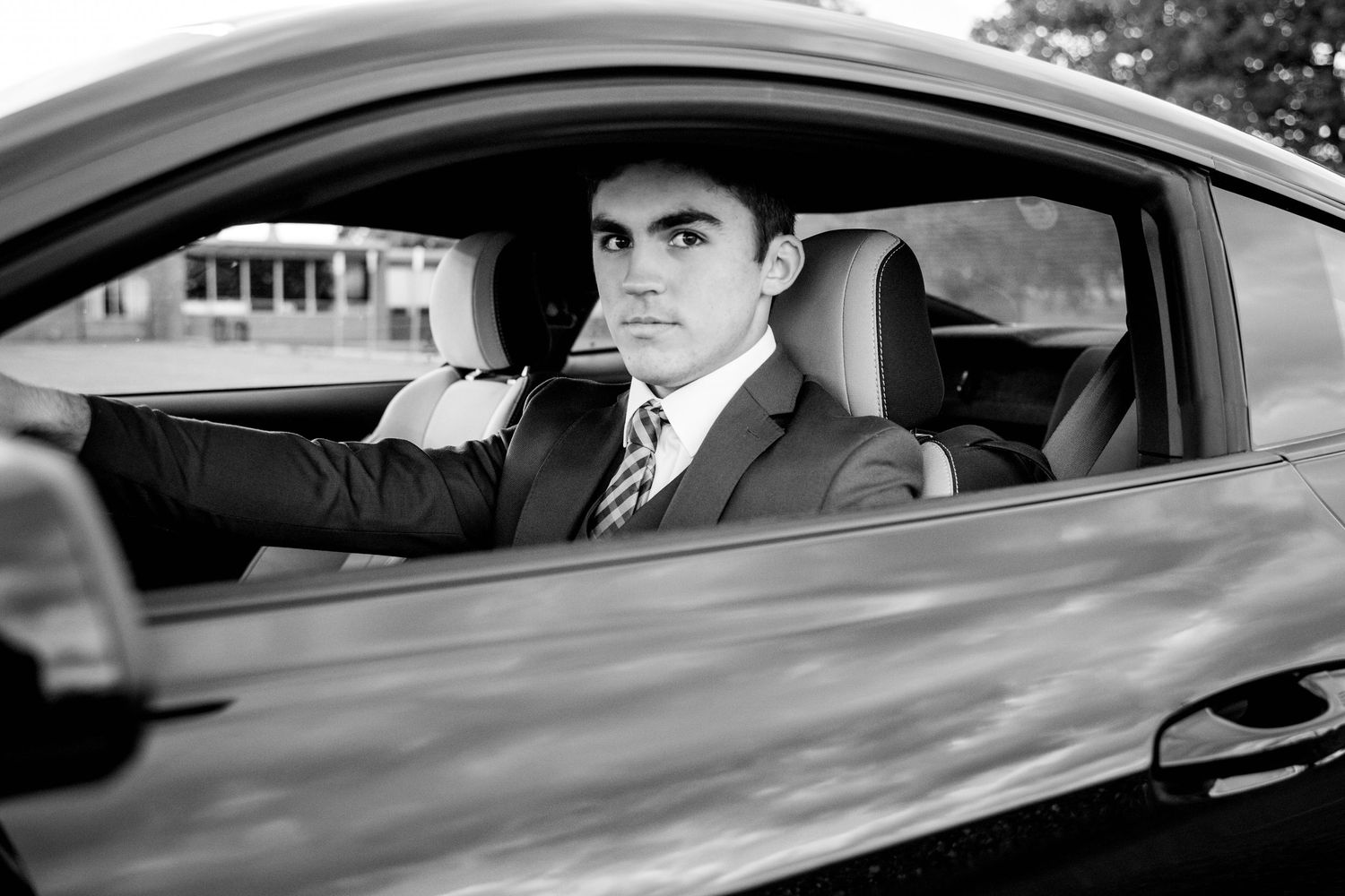 Man in suit and tie sitting in a luxury car, black and white portrait photography.