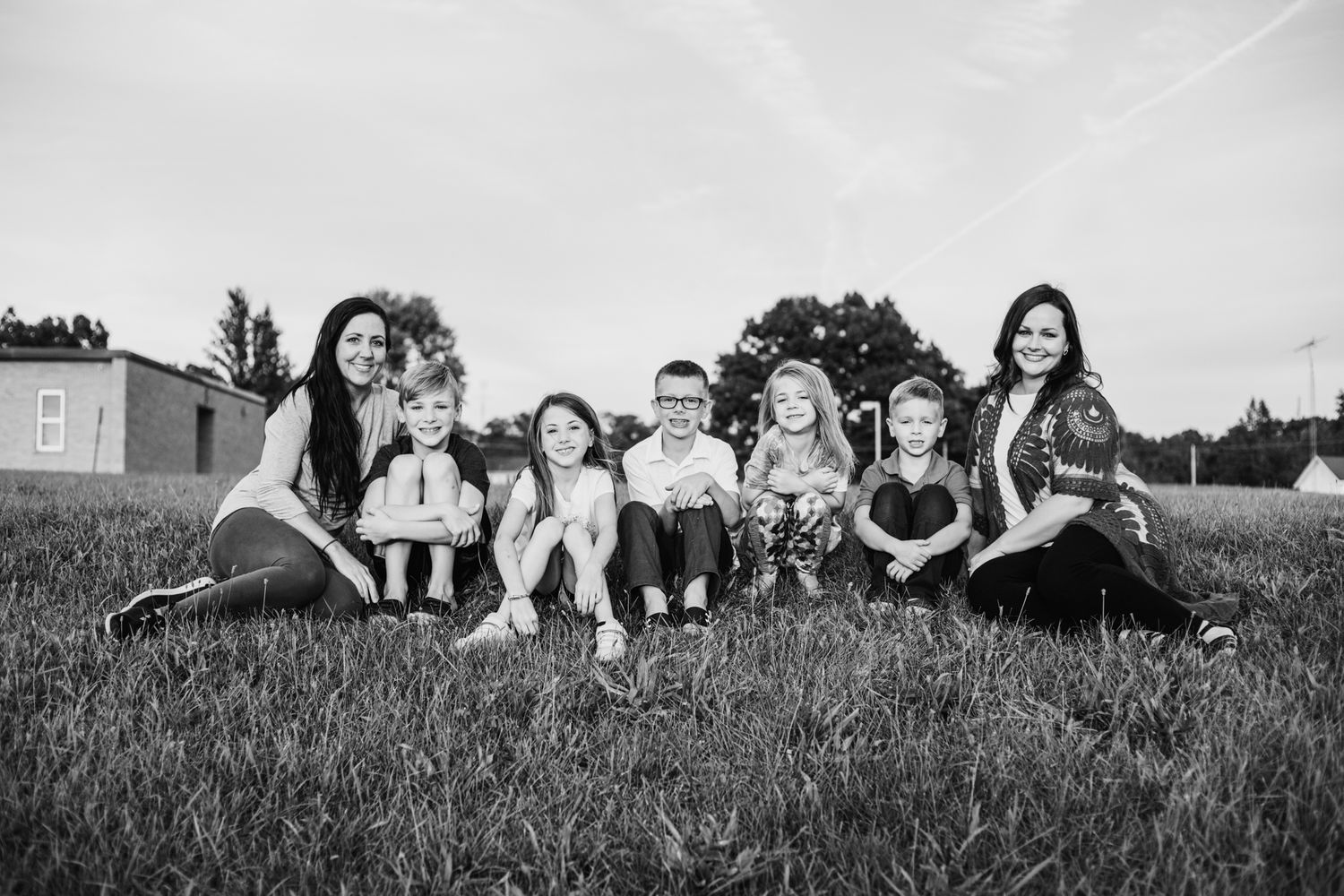 Black and white family photo of two women with five children sitting together on green grass outdoors.