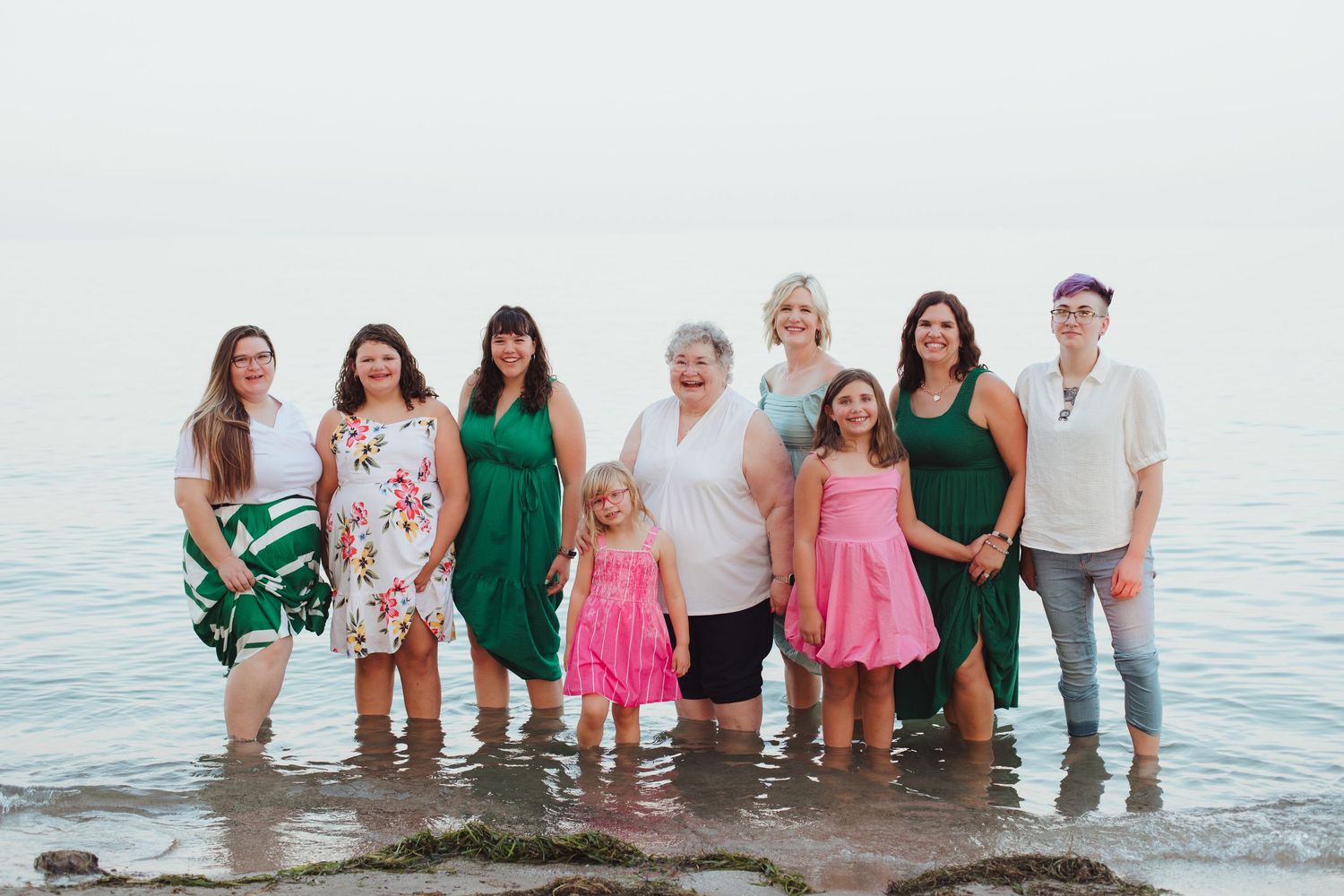 Group of women and young girls standing together in shallow water at a lakeside beach.