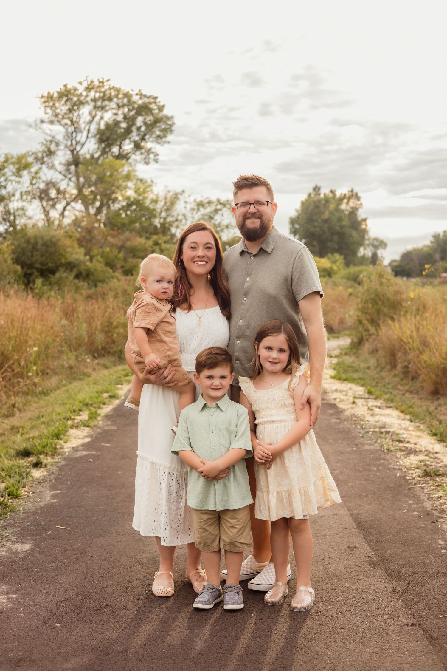 Family of five posing on a scenic path surrounded by lush greenery during a warm outdoor photo session.