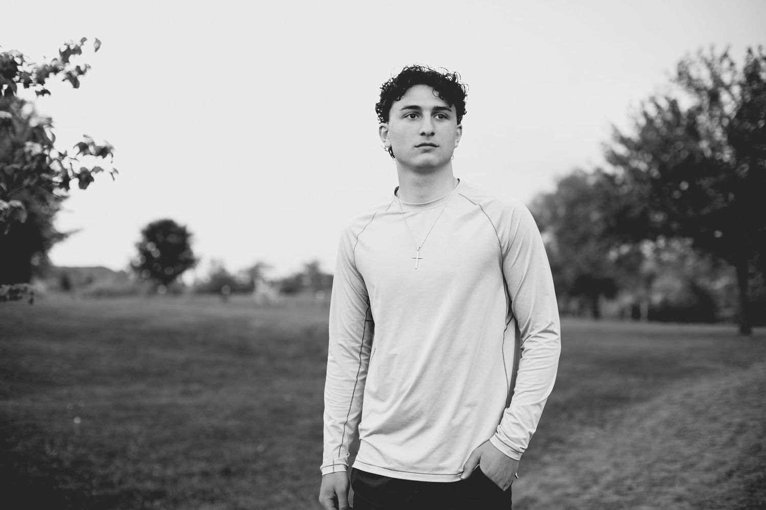 Young man in white long-sleeve shirt standing in a park, black and white portrait photography.