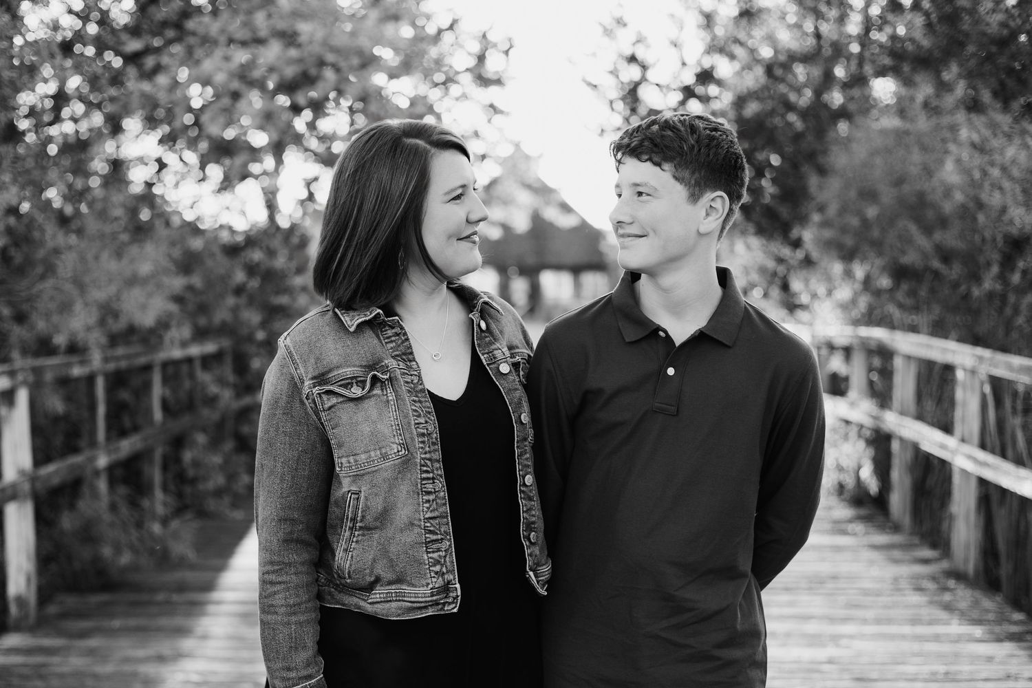 Black and white photo of a smiling young couple on a wooden bridge outdoors.