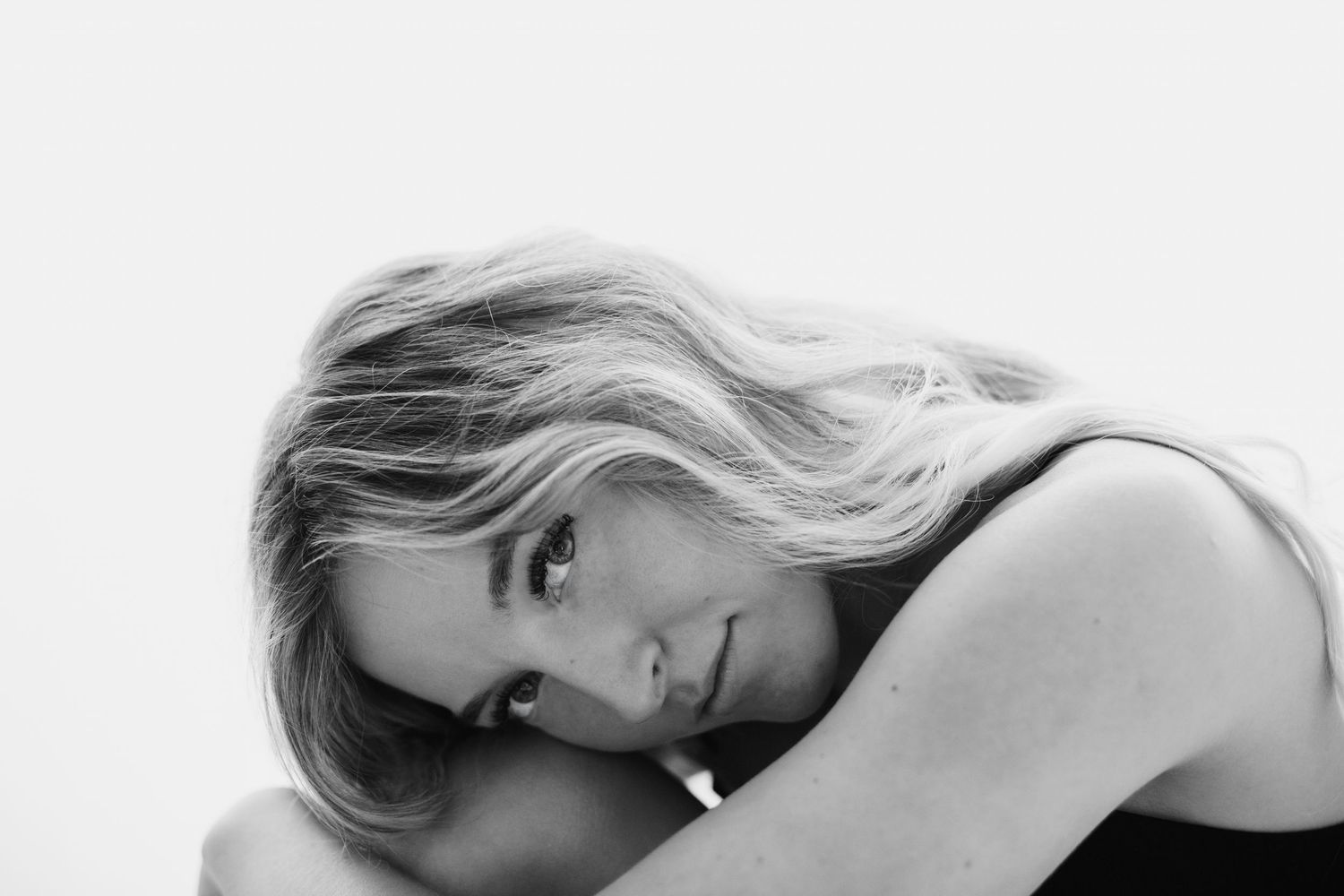 Blonde woman with flowing hair resting chin on hands in elegant black and white portrait.