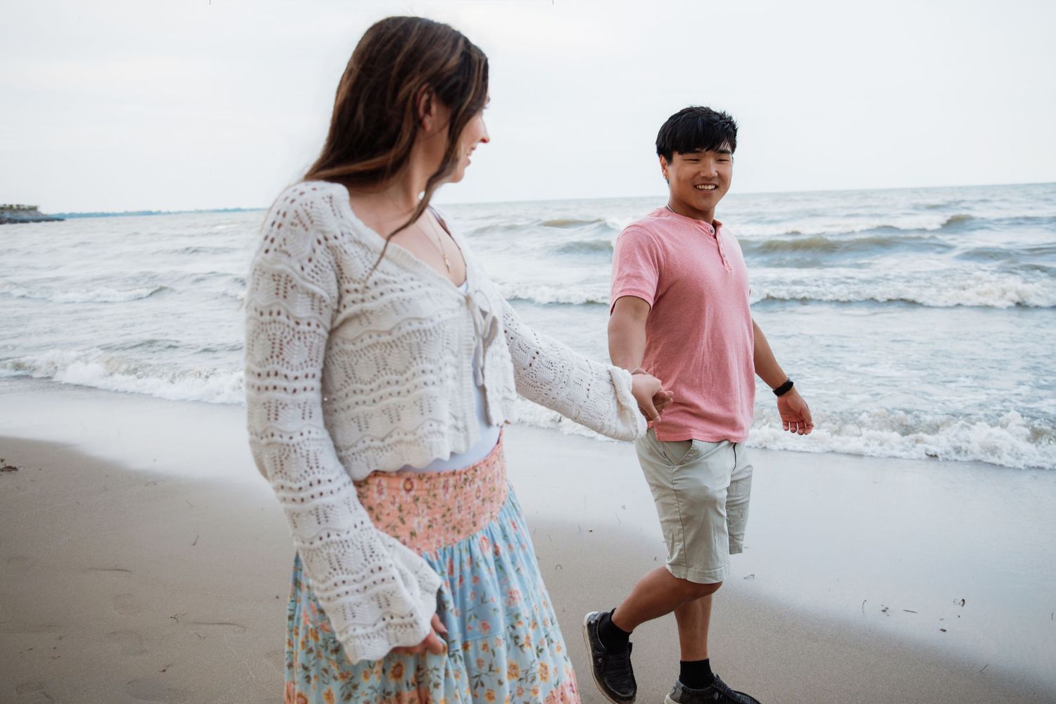 Young couple holding hands walking along ocean beach shoreline together.