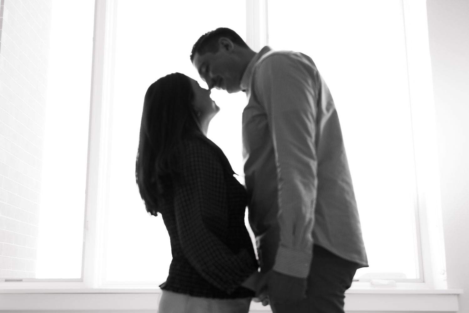 Black and white silhouette of couple sharing intimate moment by bright window.