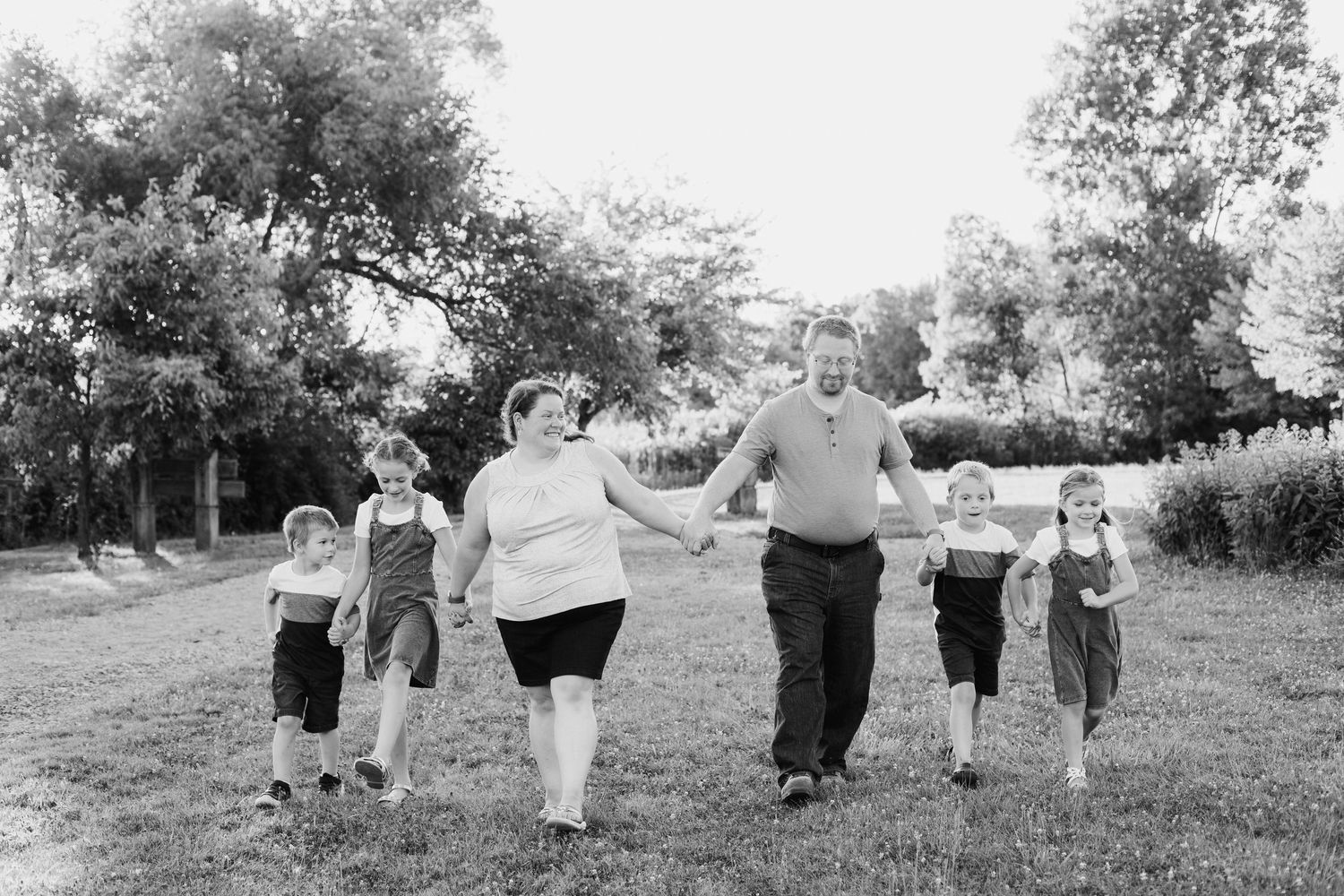 Black and white photo of a family holding hands and walking together on a grassy lawn outdoors.