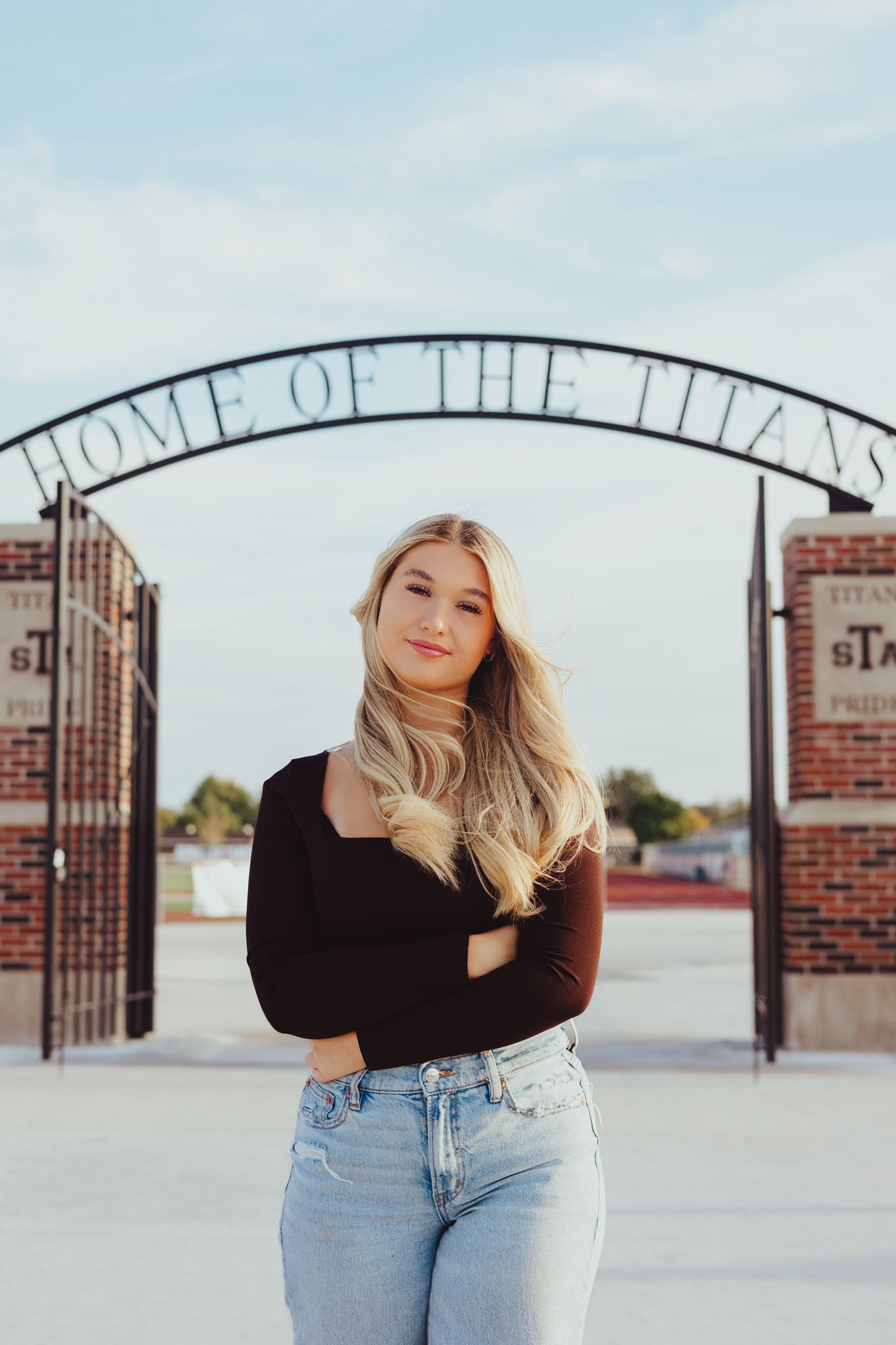 Blonde teenage girl in black top and jeans posing before Home of the Titans arch.