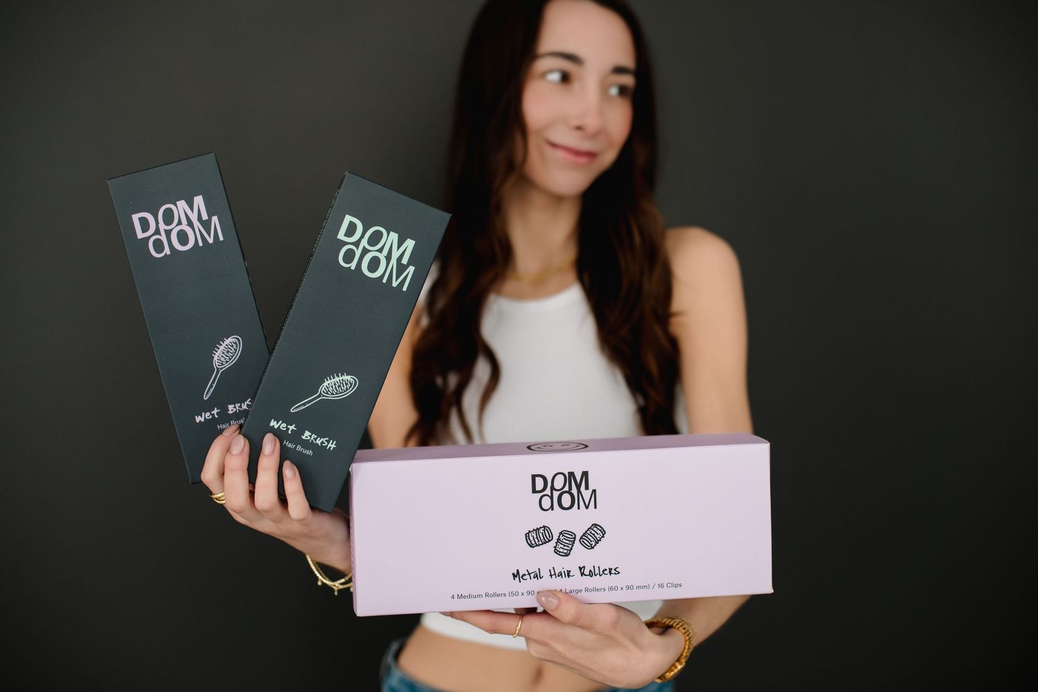 Woman holding Dom Dom hair product boxes and pink kit against dark background.
