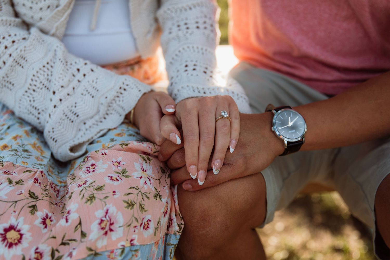 Close-up of couple holding hands showing engagement ring and watch during outdoor engagement photo session.