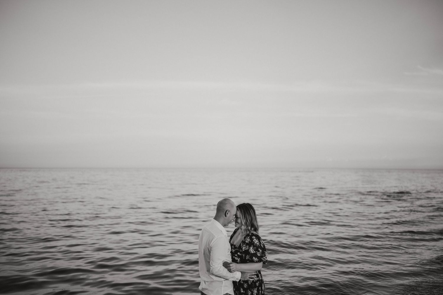 Black and white minimalist photo of a couple facing each other against a vast ocean backdrop.
