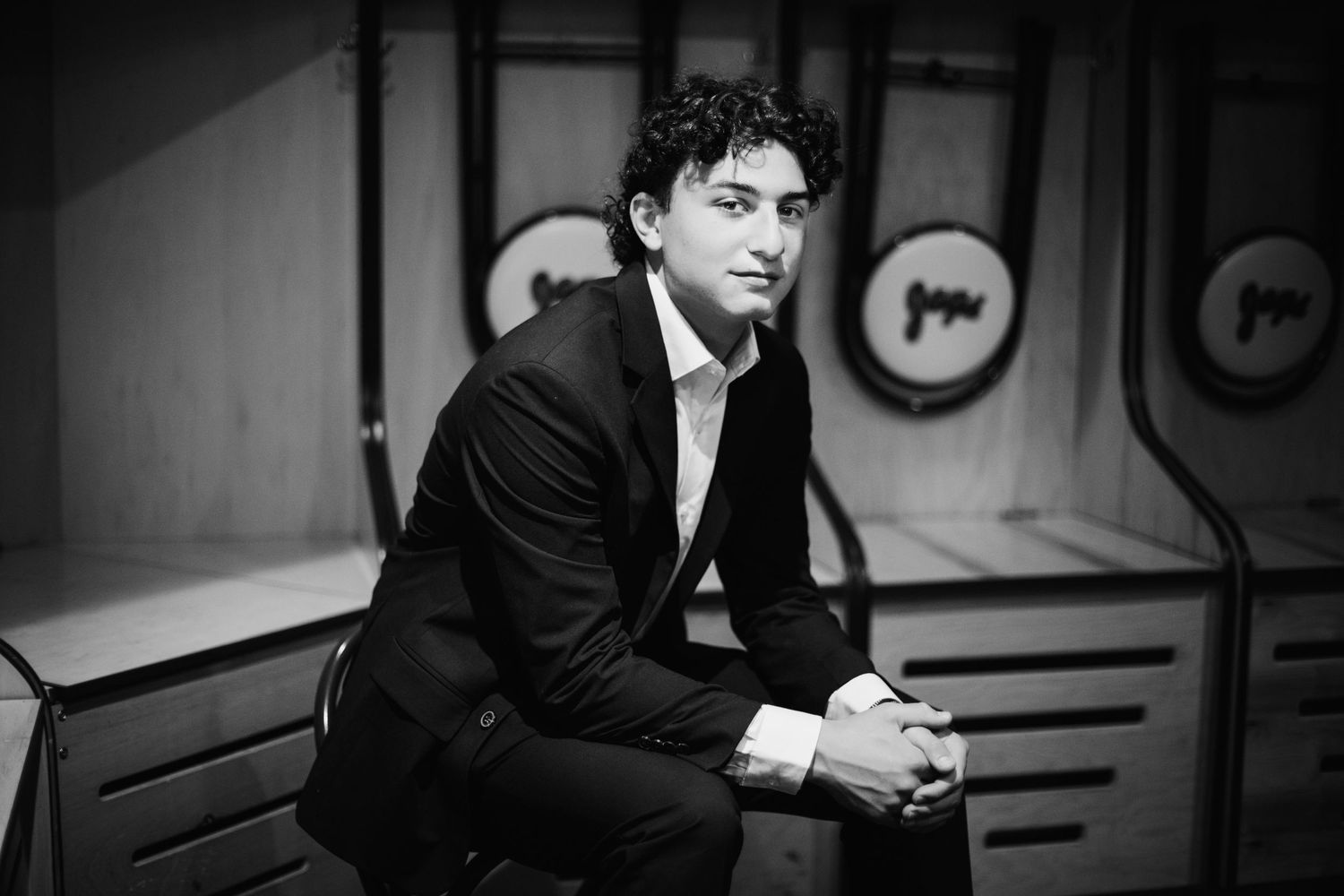 Young man in a black suit sitting pensively in a black and white portrait photo.