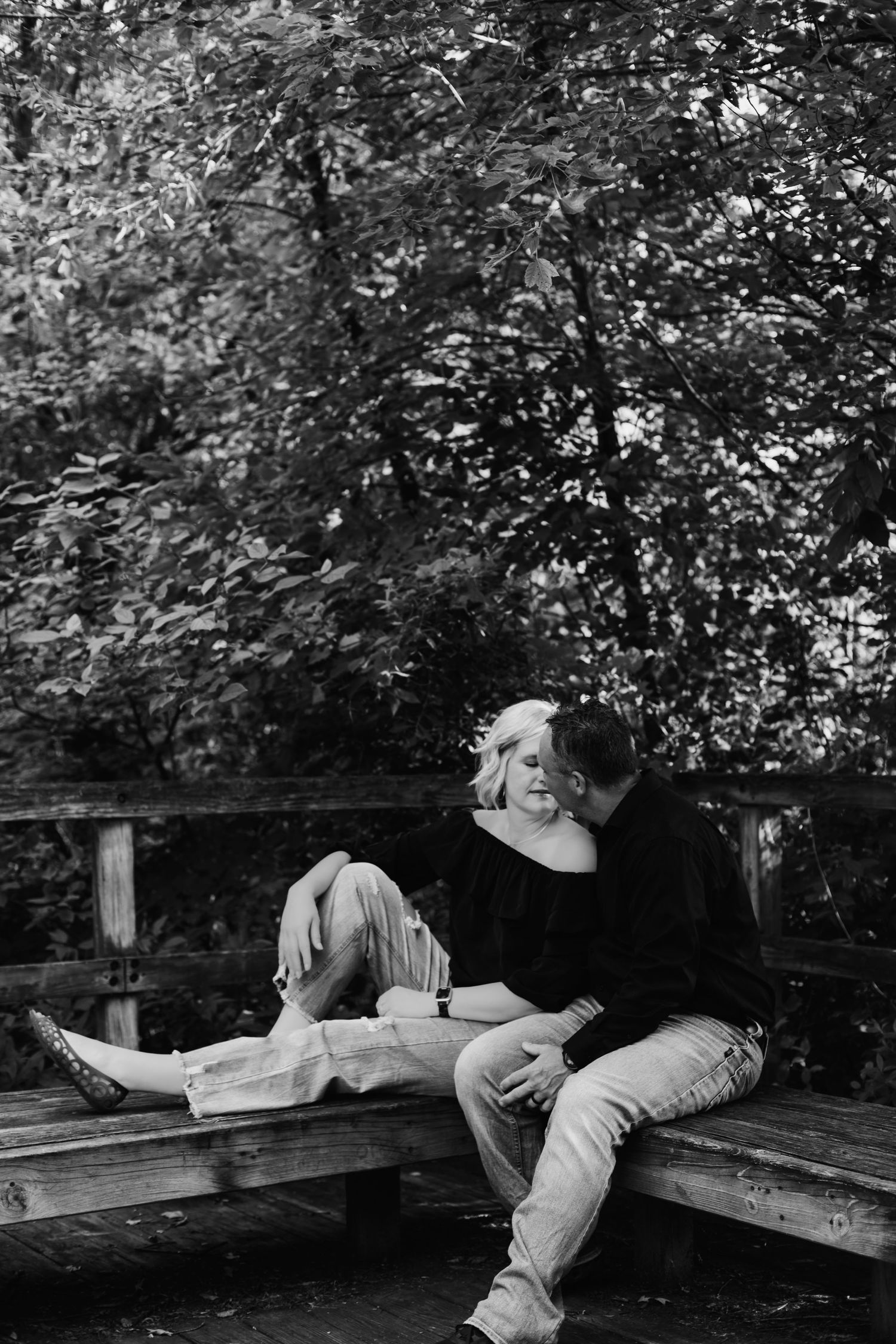 Black and white photo of couple sitting close together on a wooden bench outdoors.