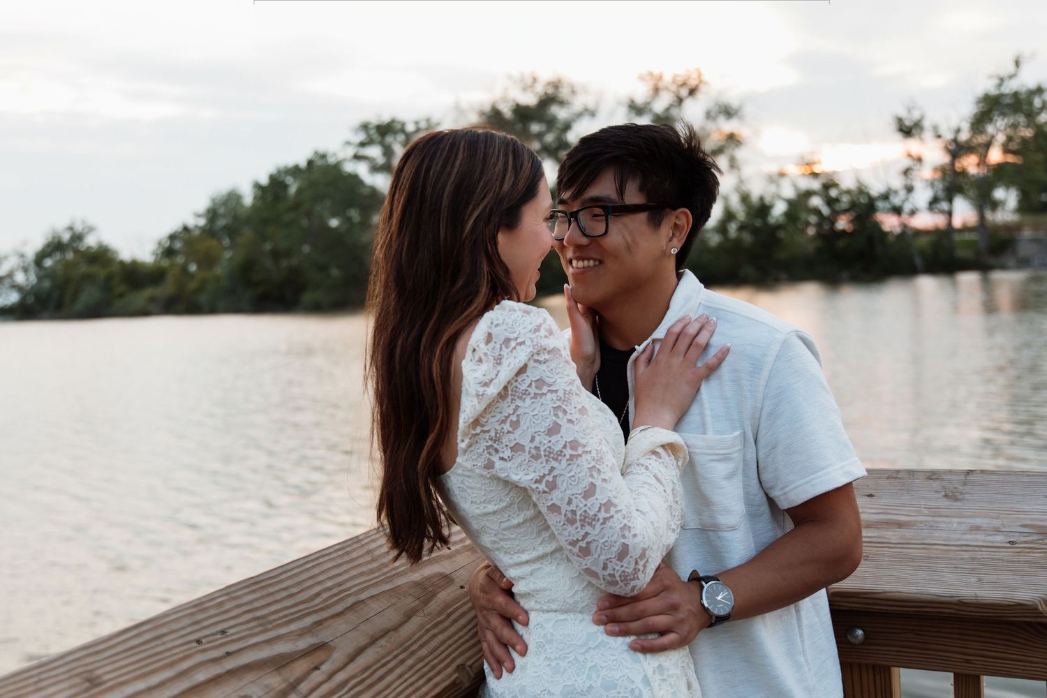 Couple sharing a romantic moment on a lakeside dock, nearly kissing at golden hour.
