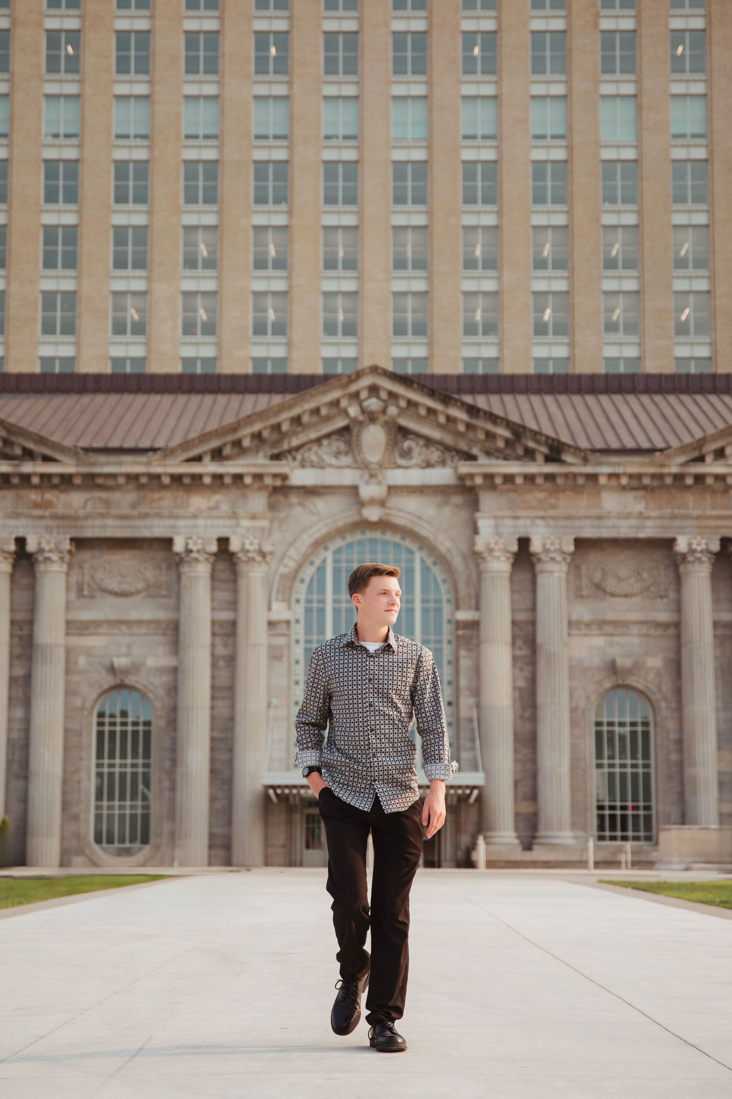Young man in patterned shirt walks confidently in front of a large neoclassical building.