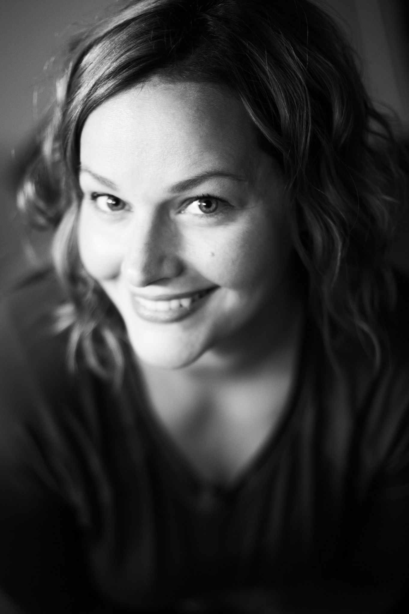Close-up black and white portrait of smiling woman with wavy hair and warm expression.