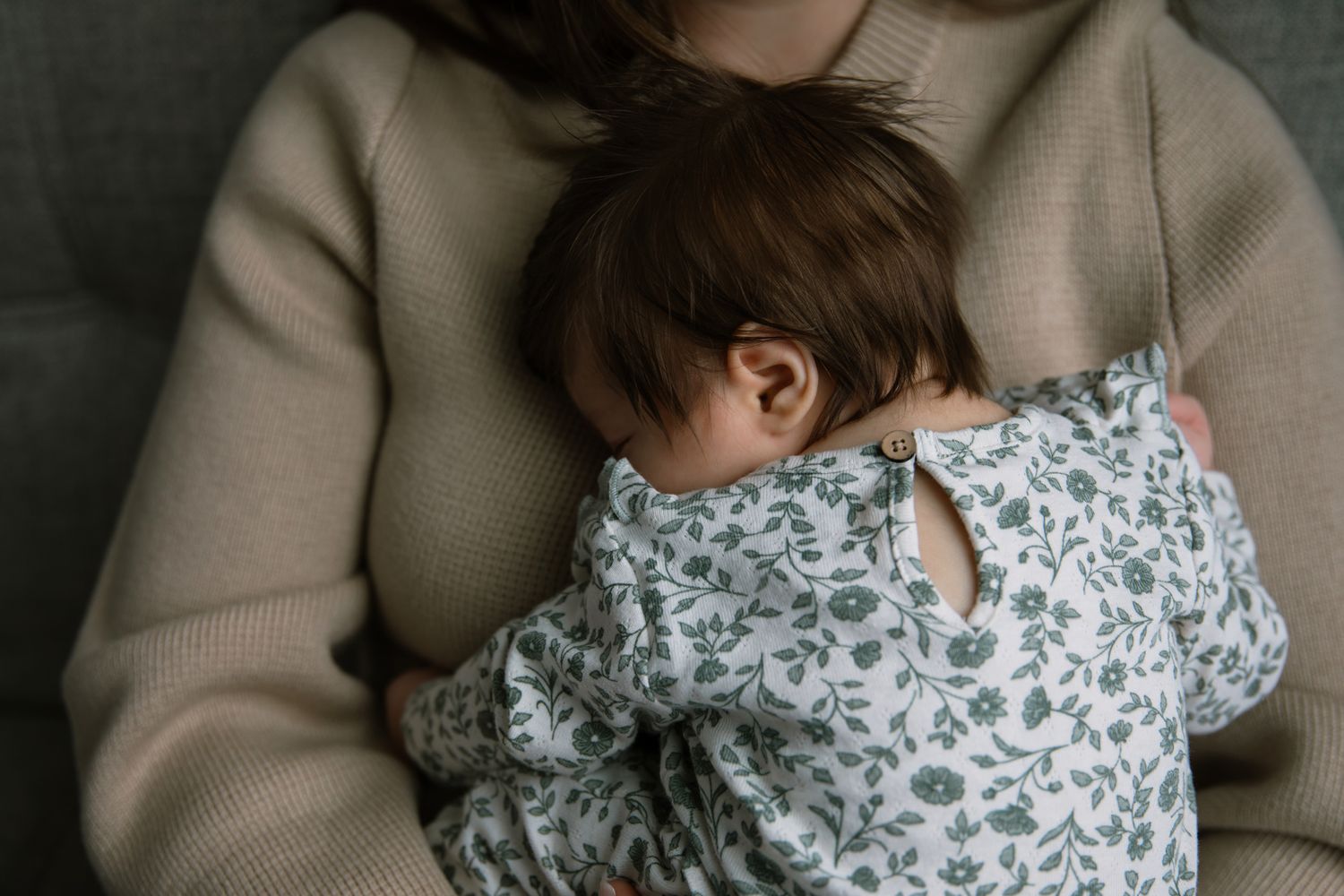 Mother in beige sweater cradling newborn baby in floral onesie.