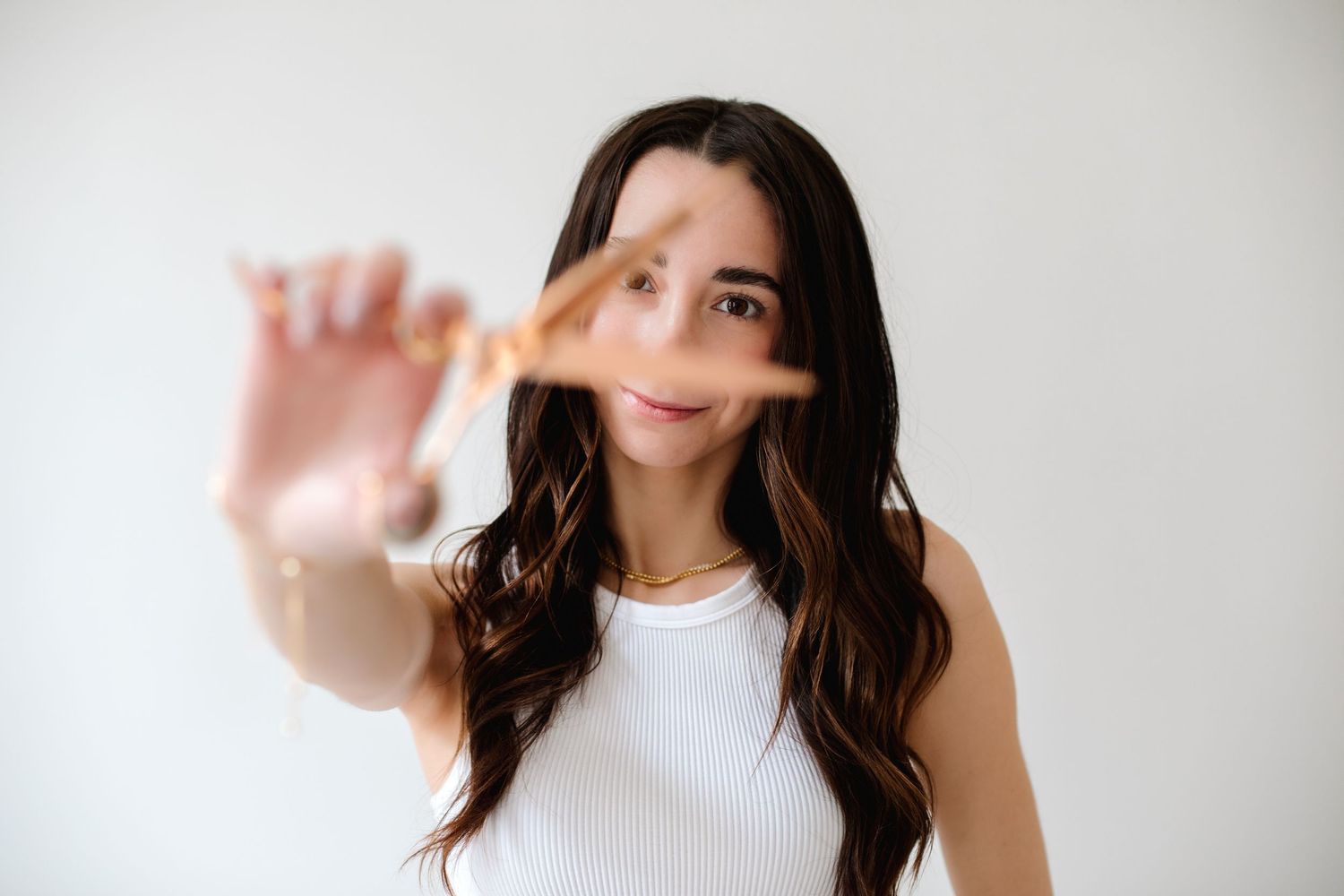 Young woman in white top holding makeup brush toward camera in bright studio setting.