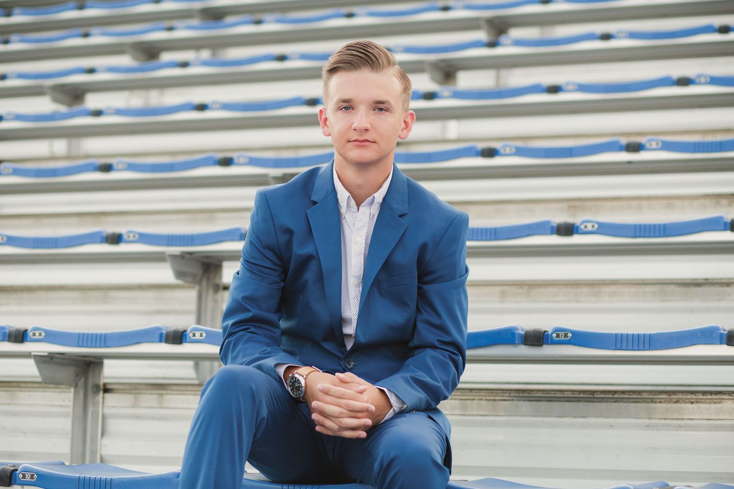 Young man in blue suit sitting on stadium bleachers, posing confidently for a formal portrait photo.