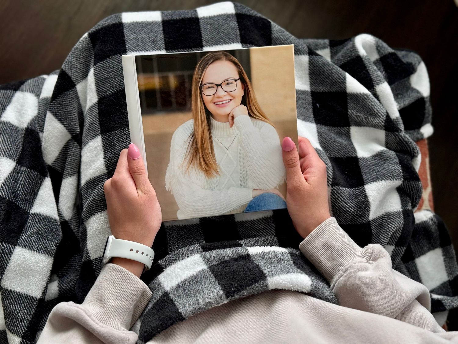 Child holding printed portrait photo of smiling teenage girl wearing glasses and white sweater.