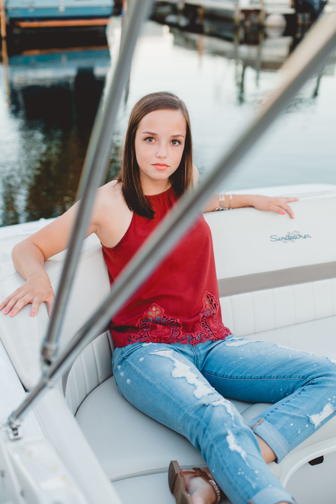Young woman in red top and ripped jeans sitting relaxed on a white boat at a marina.