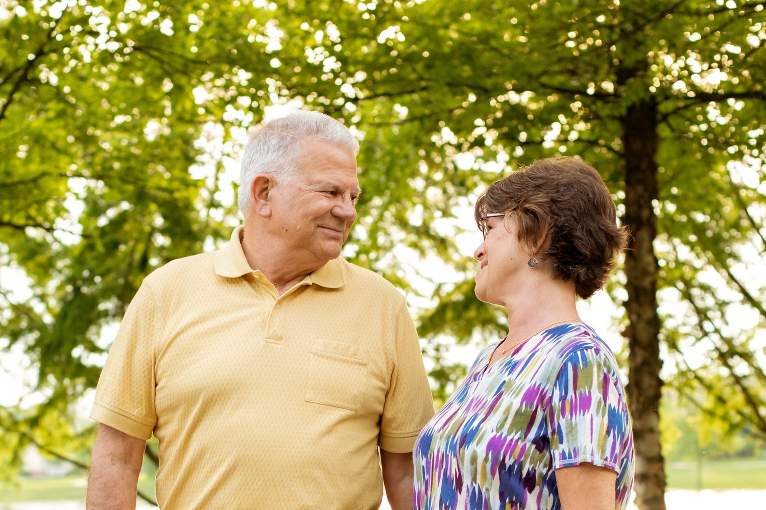 Smiling senior couple enjoying a sunny day outdoors in a lush green park, looking at each other affectionately.