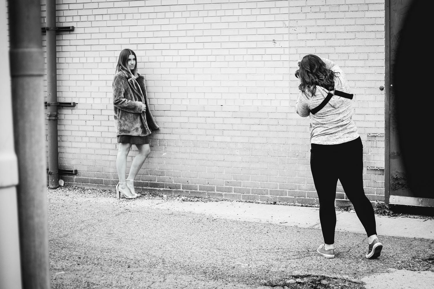 Photographer captures a young woman posing against a brick wall outdoors.