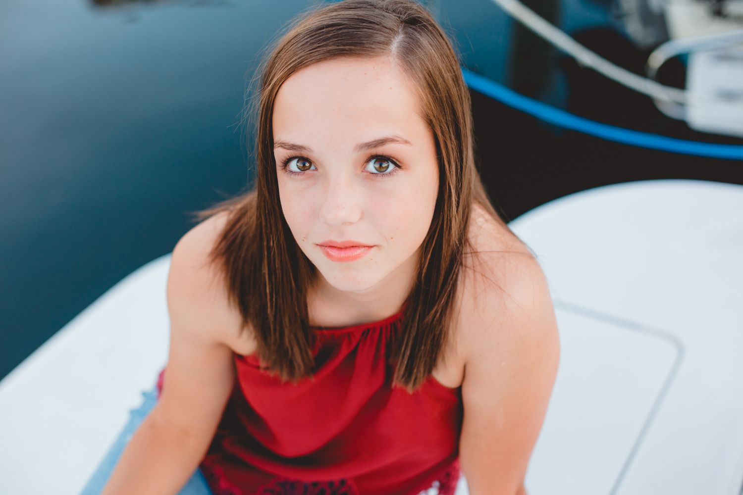 Young woman in red dress sitting on a white boat with blue water in the background.