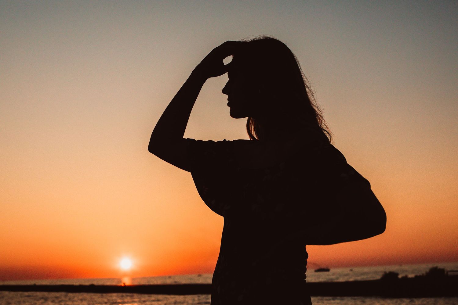 Silhouette of a woman posing against a vibrant orange sunset over the ocean.