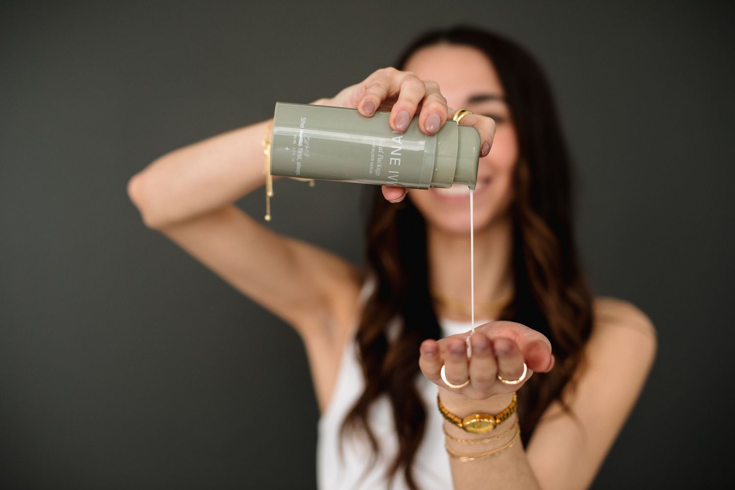 Woman pouring product from olive green container into her hand against dark background.