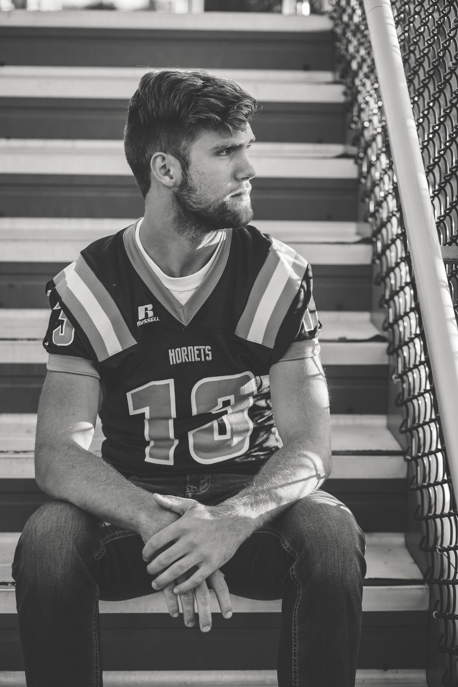 Black and white photo of a young man in a Hornets football jersey number 13 sitting on bleachers.
