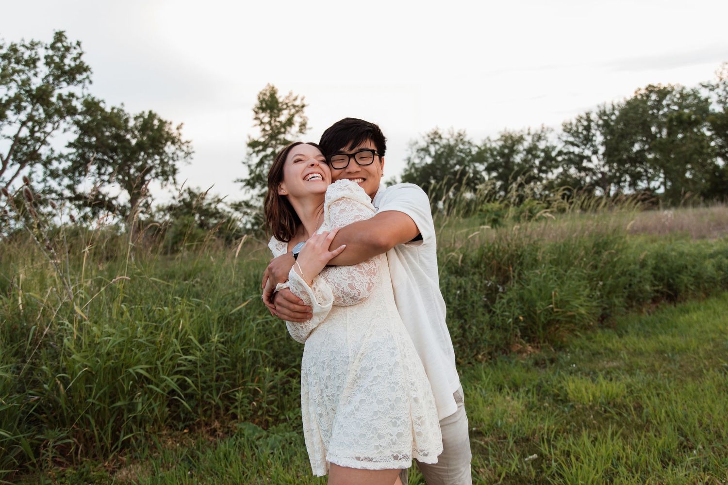 Happy couple embracing and laughing together in a lush green meadow field outdoors.