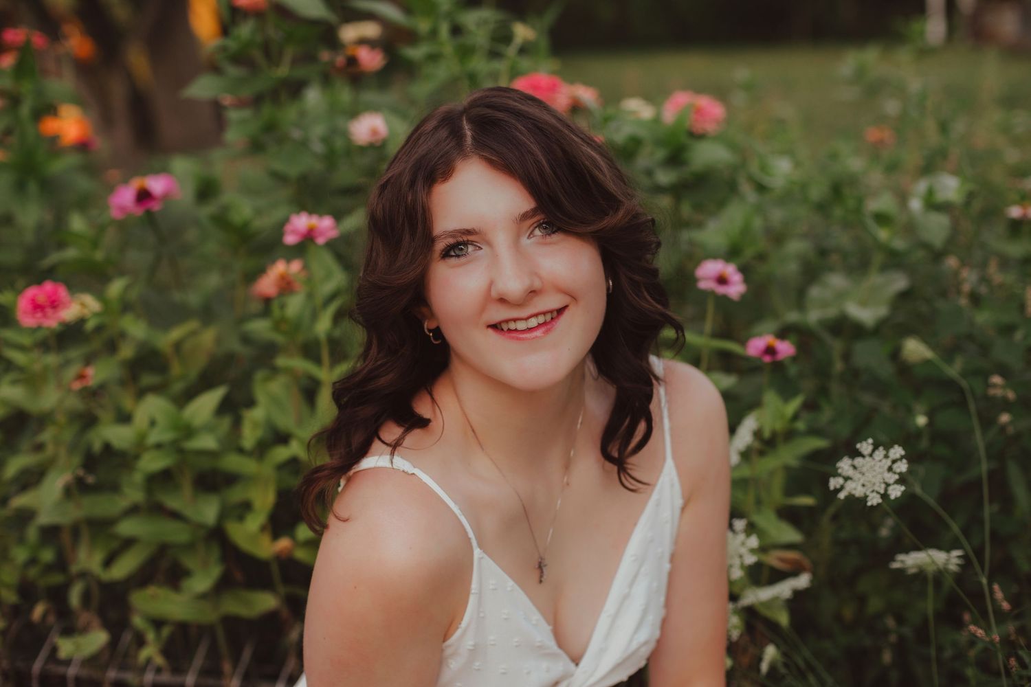 Smiling young brunette woman sitting among colorful pink and orange flowers in a garden.