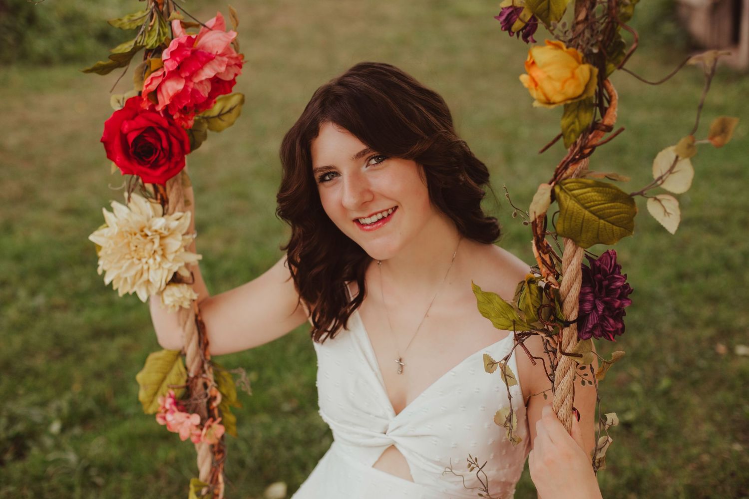 Smiling young woman in white dress sitting on a floral decorated wooden swing.
