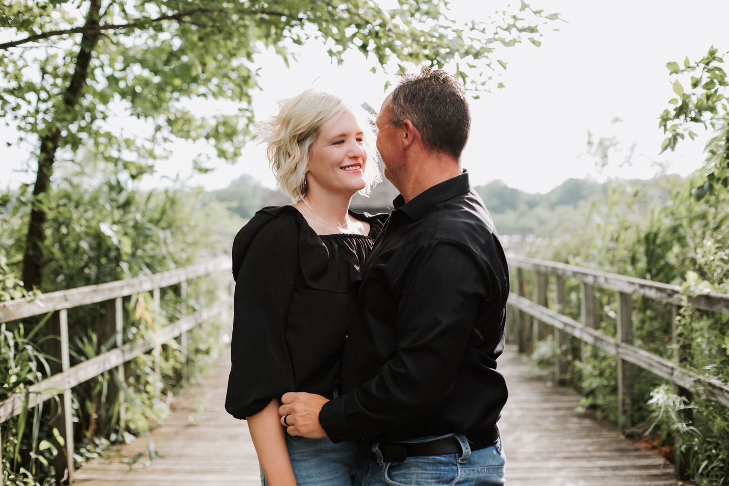 Couple sharing a romantic moment on a wooden bridge surrounded by green trees.