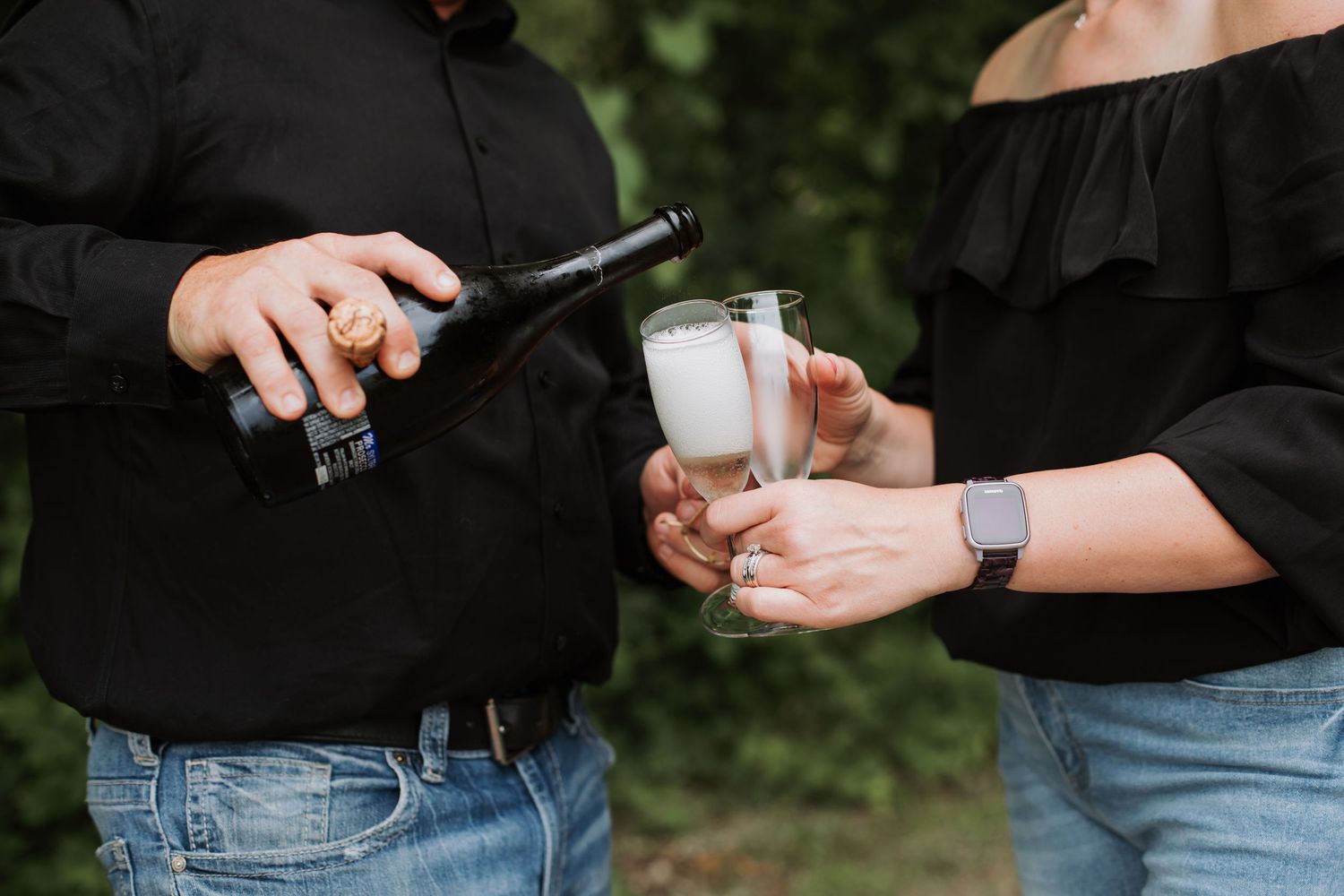 Couple pouring champagne into glasses outdoors in a garden setting.