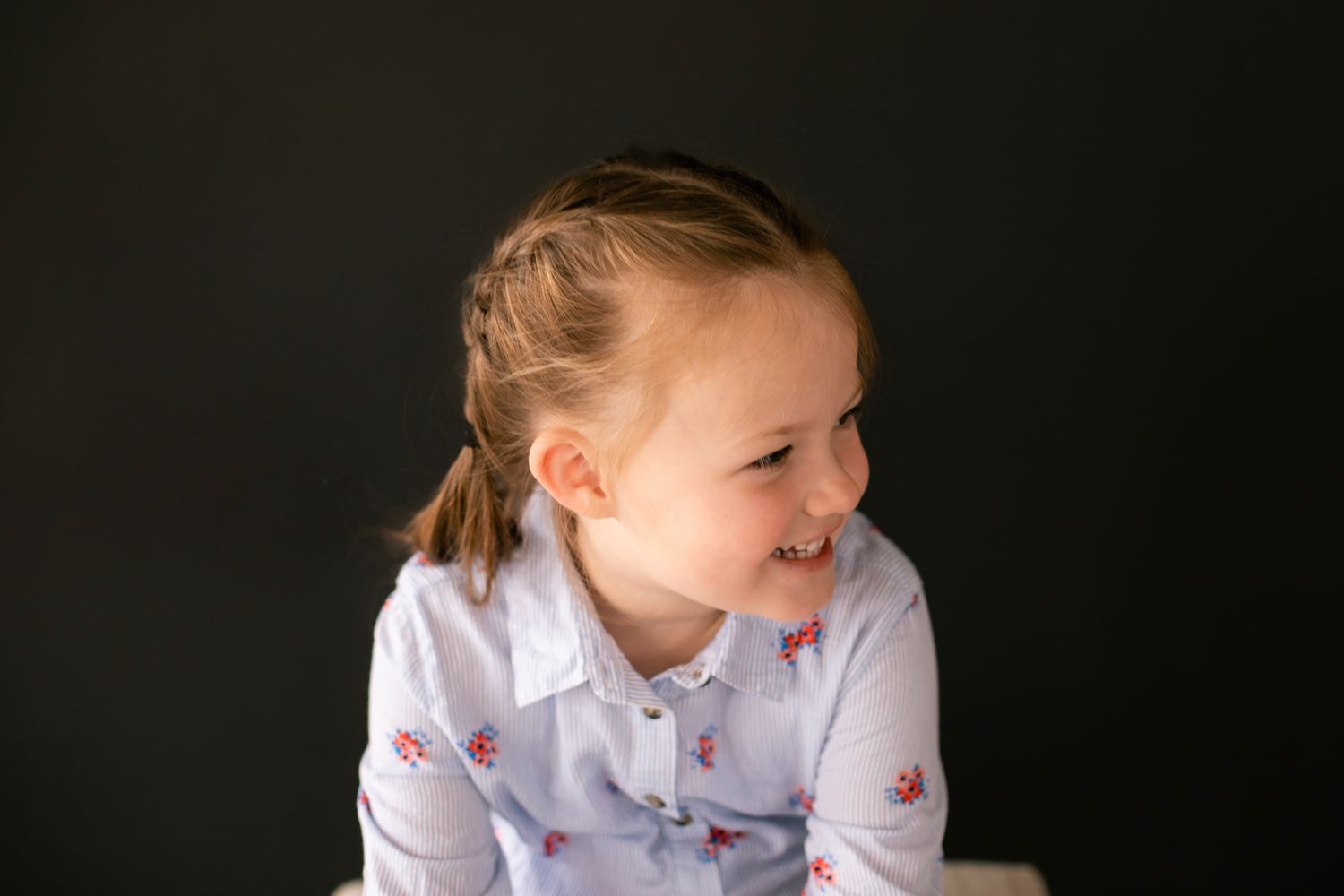 Happy young girl with braided hair laughs while looking to the side against a dark background.