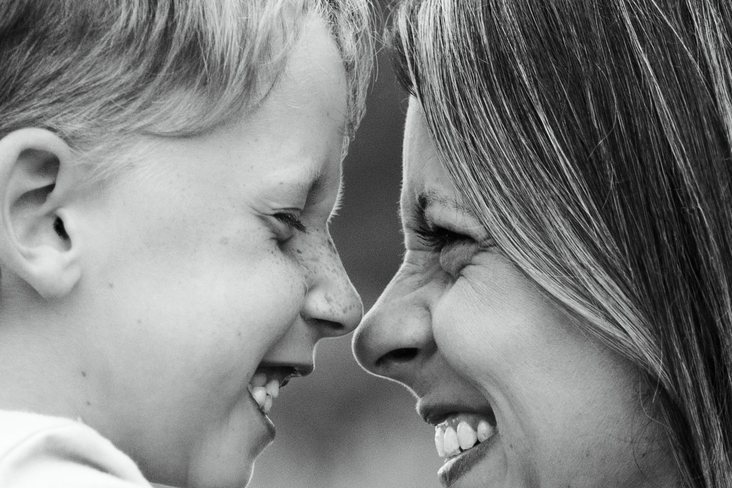 Black and white portrait of laughing mother and young child touching noses joyfully.