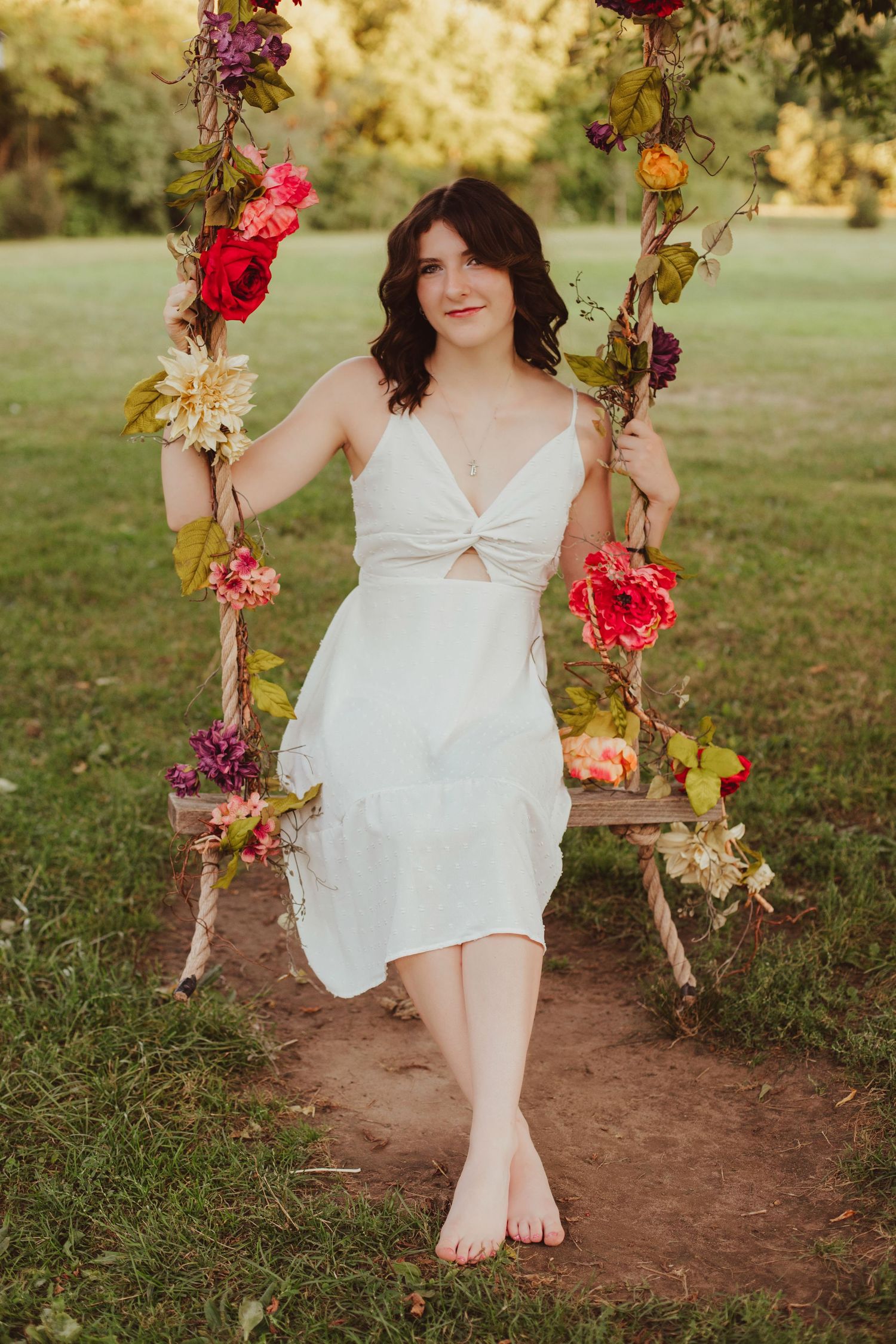 Young woman in white dress sitting on a colorful floral swing in green park.