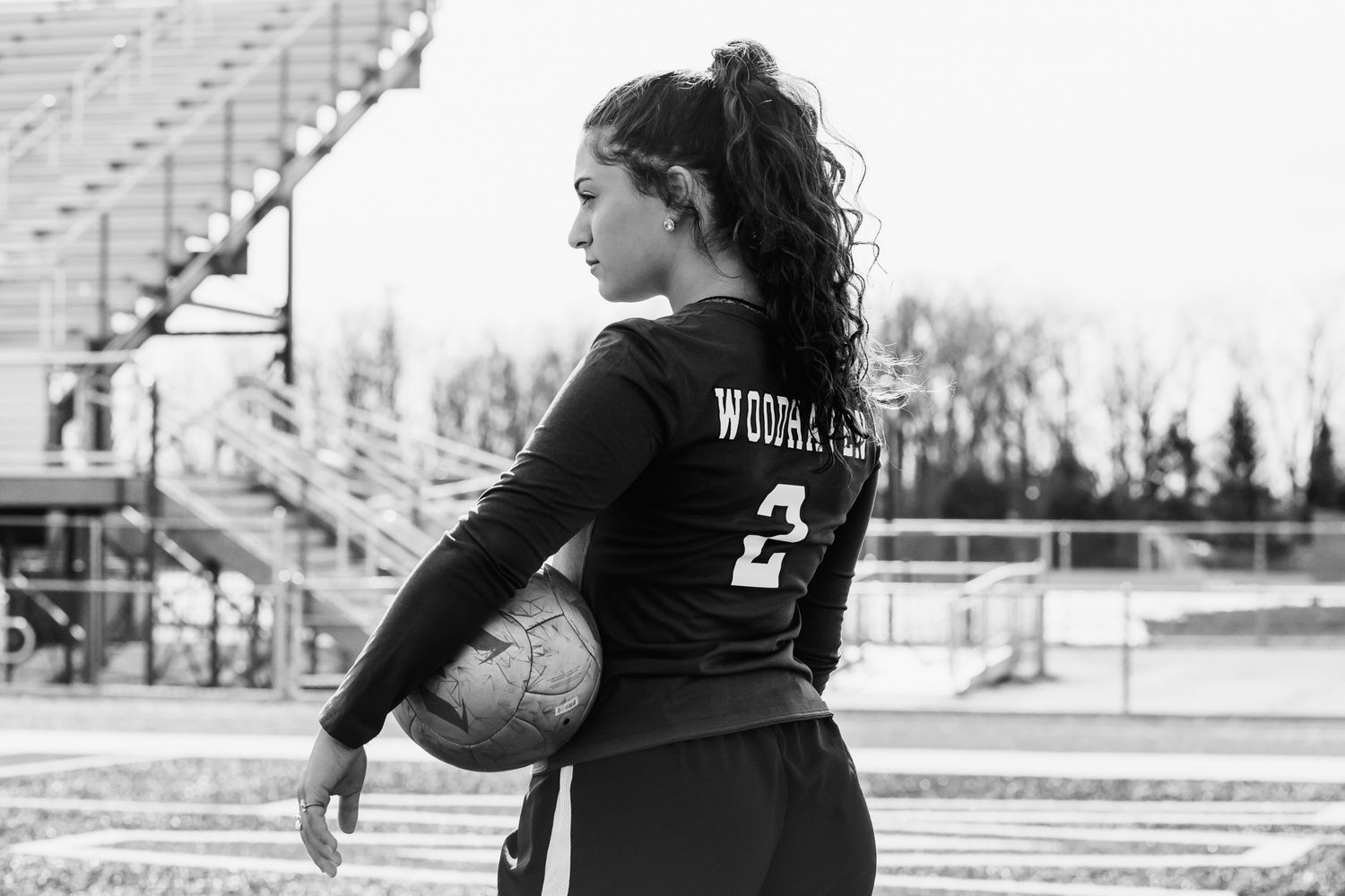 Teenage female soccer player holds ball showing Woodhaven Warriors jersey number 2 in black and white.