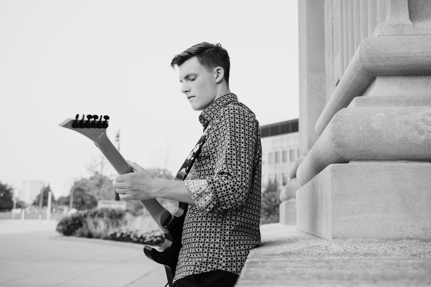 Black and white photo of young man playing electric guitar near column.