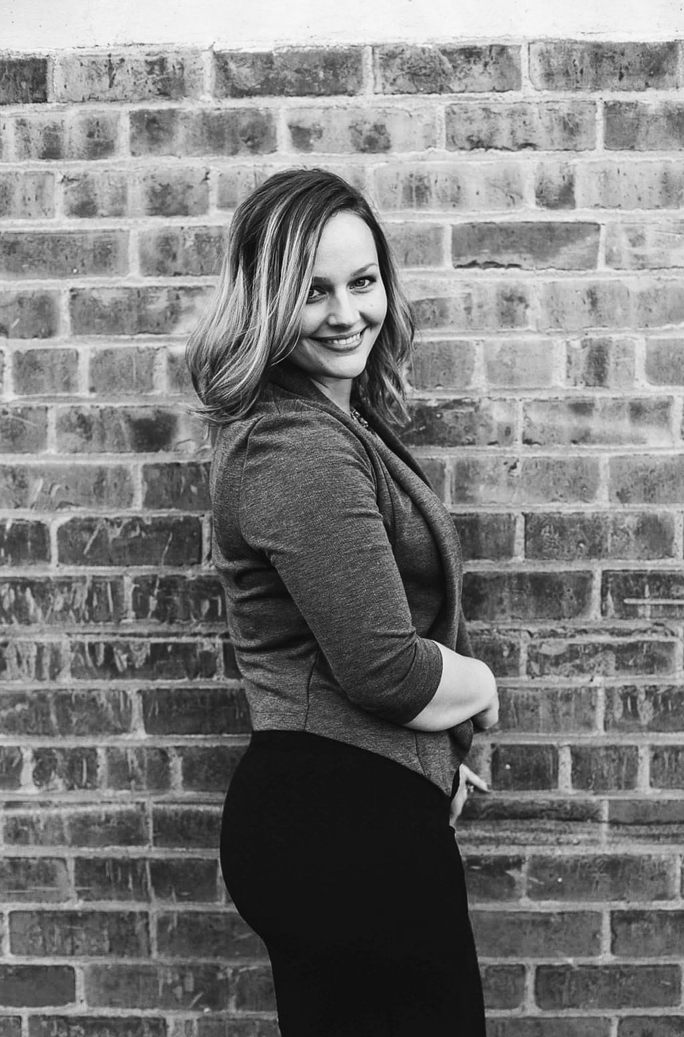 Smiling woman posing against brick wall in black and white portrait photography.