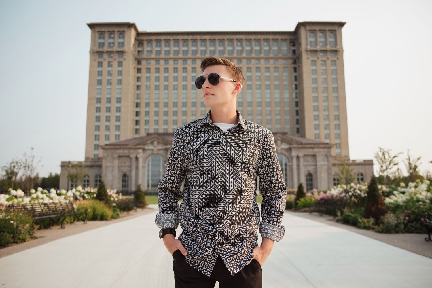 Young man in patterned shirt and sunglasses posing before a grand historic building.