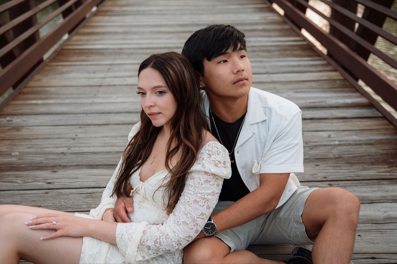 A young couple sits together on a wooden bridge, the woman leaning back against the man.
