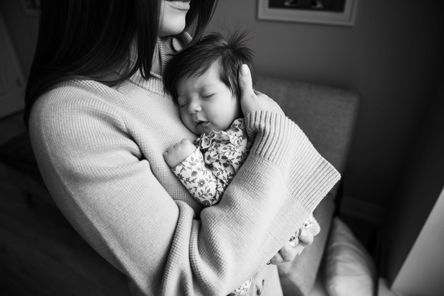 Black and white photo of a mother cradling her sleeping newborn baby wrapped in a floral blanket.