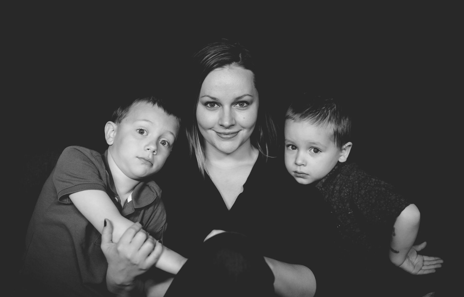 Black and white portrait of a smiling woman with two young boys against a dark background.